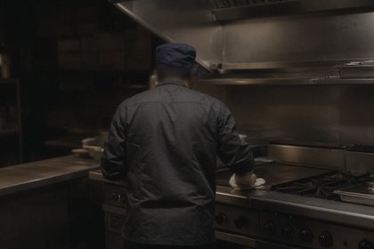A cook, seen from behind, wipes down a steel line at night